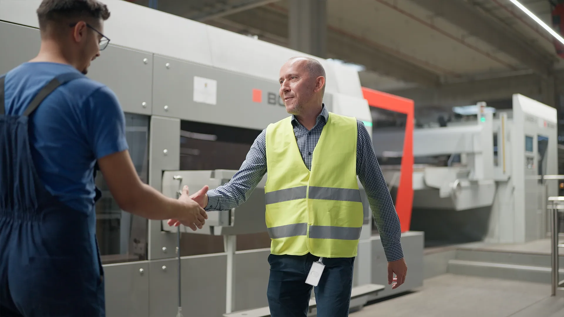 Mihai Radu shaking hands with an operator in front of the BOBST die-cutter